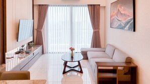 A modern living room with a sofa, a coffee table, a TV, and a painting on the wall. - Big Spacious and Homey 3BR at Sky House BSD Apartment (Pagedangan)