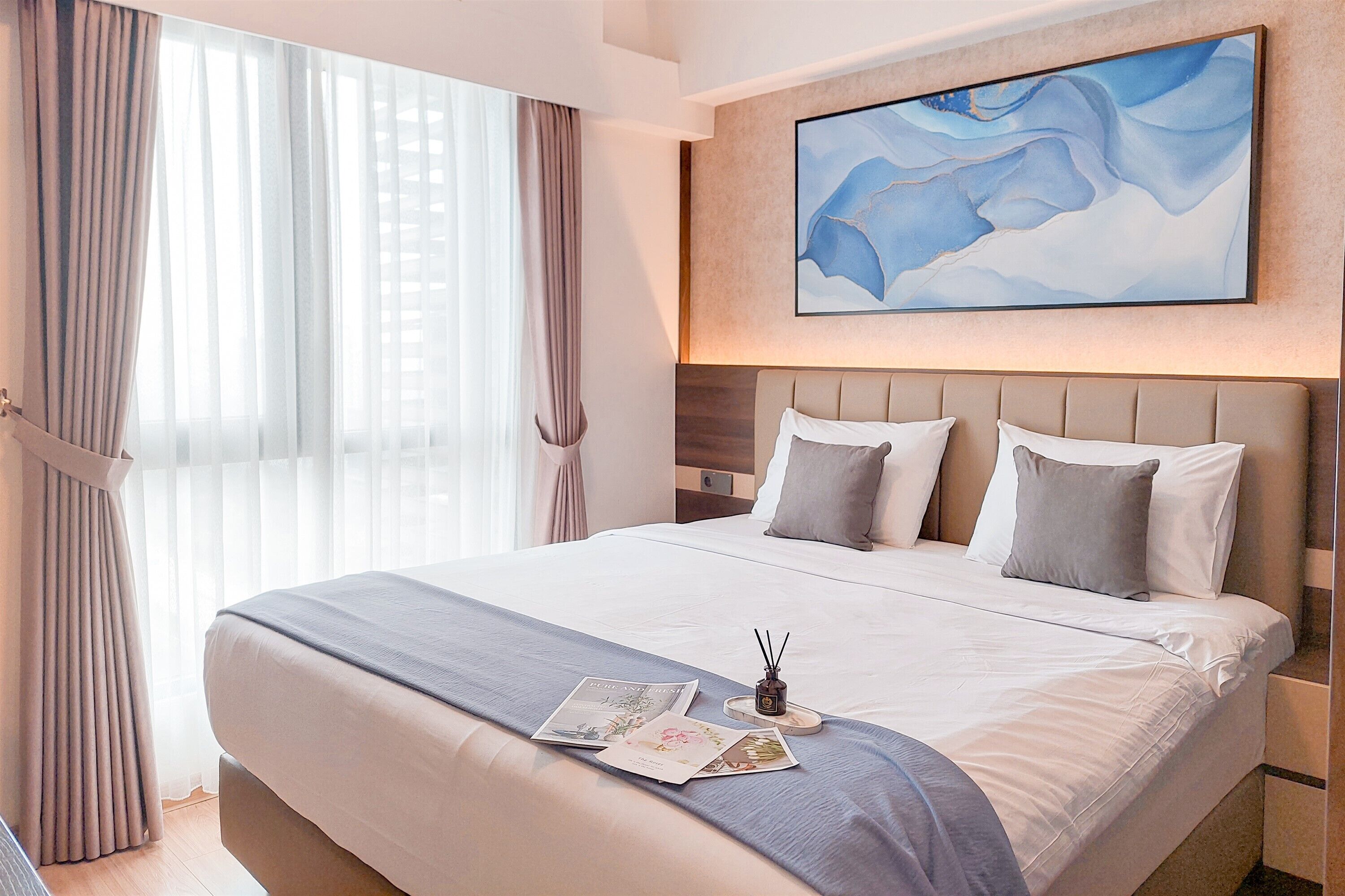 A hotel room with a large bed, a headboard, and a painting on the wall.
