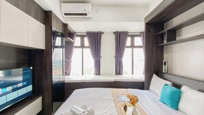 A hotel room with a bed, a TV on a stand, a window with curtains, and a tray with a vase of flowers.
