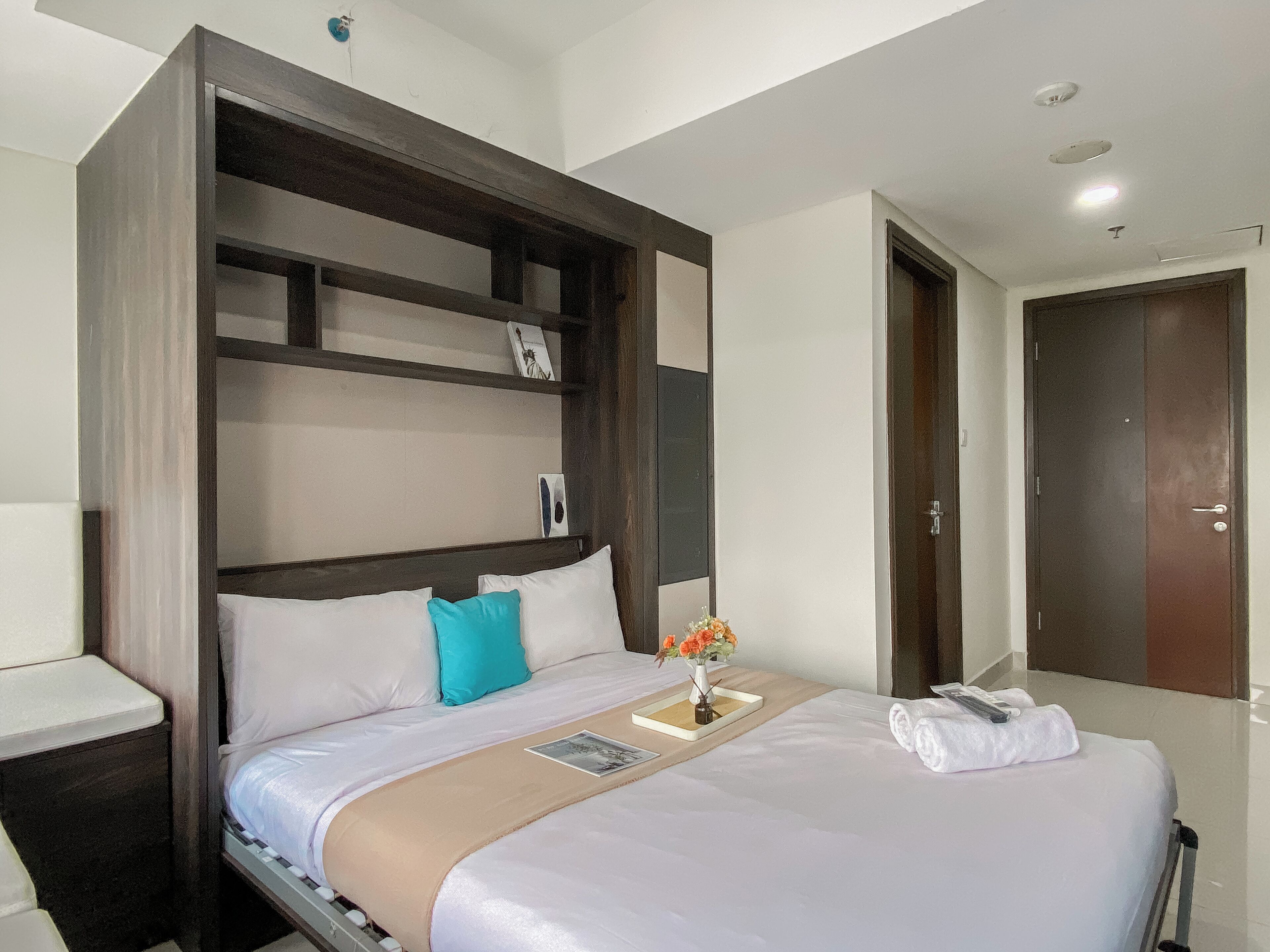 A modern hotel room with a large bed, a bedside table, a nightstand, a wardrobe, and a bathroom door.