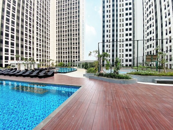 Un hotel moderno con piscina, sillas de descanso y edificios altos al fondo.