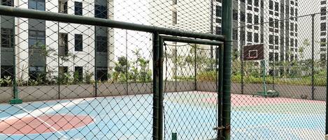 Una cancha de baloncesto rodeada por una valla de alambre con un aro de baloncesto visible al fondo.