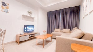 A modern living room with a sofa, a coffee table, a TV, and a curtain. - Good Deal and Restful 1BR at Branz BSD City Apartment (Pagedangan)