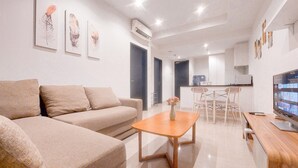 A modern living room with a sofa, coffee table, and a TV. There is a kitchen area with a dining table and chairs. - Good Deal and Restful 1BR at Branz BSD City Apartment (Pagedangan)