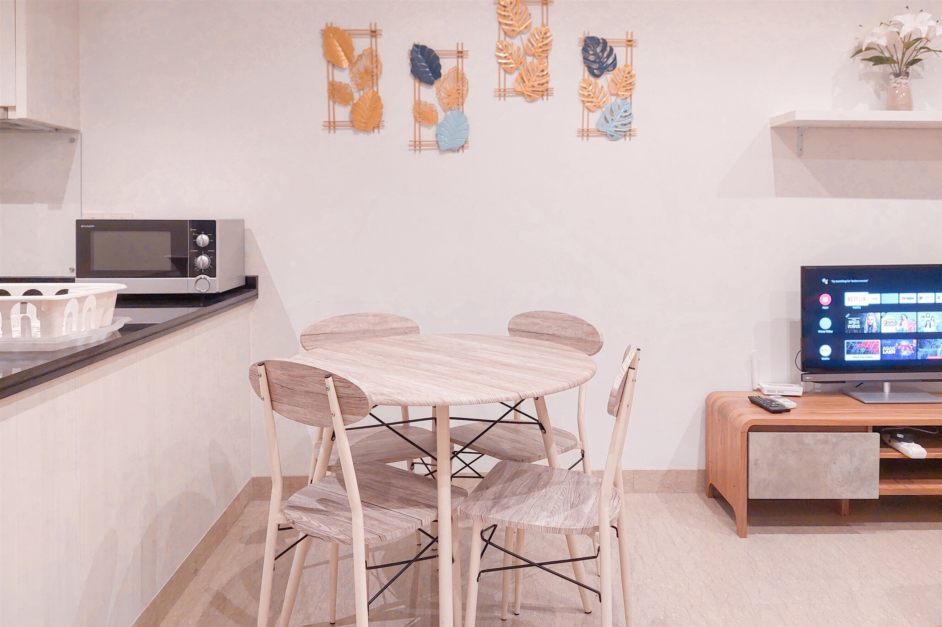 A modern kitchen with a microwave, a dining table with chairs, and a TV on a wooden stand.