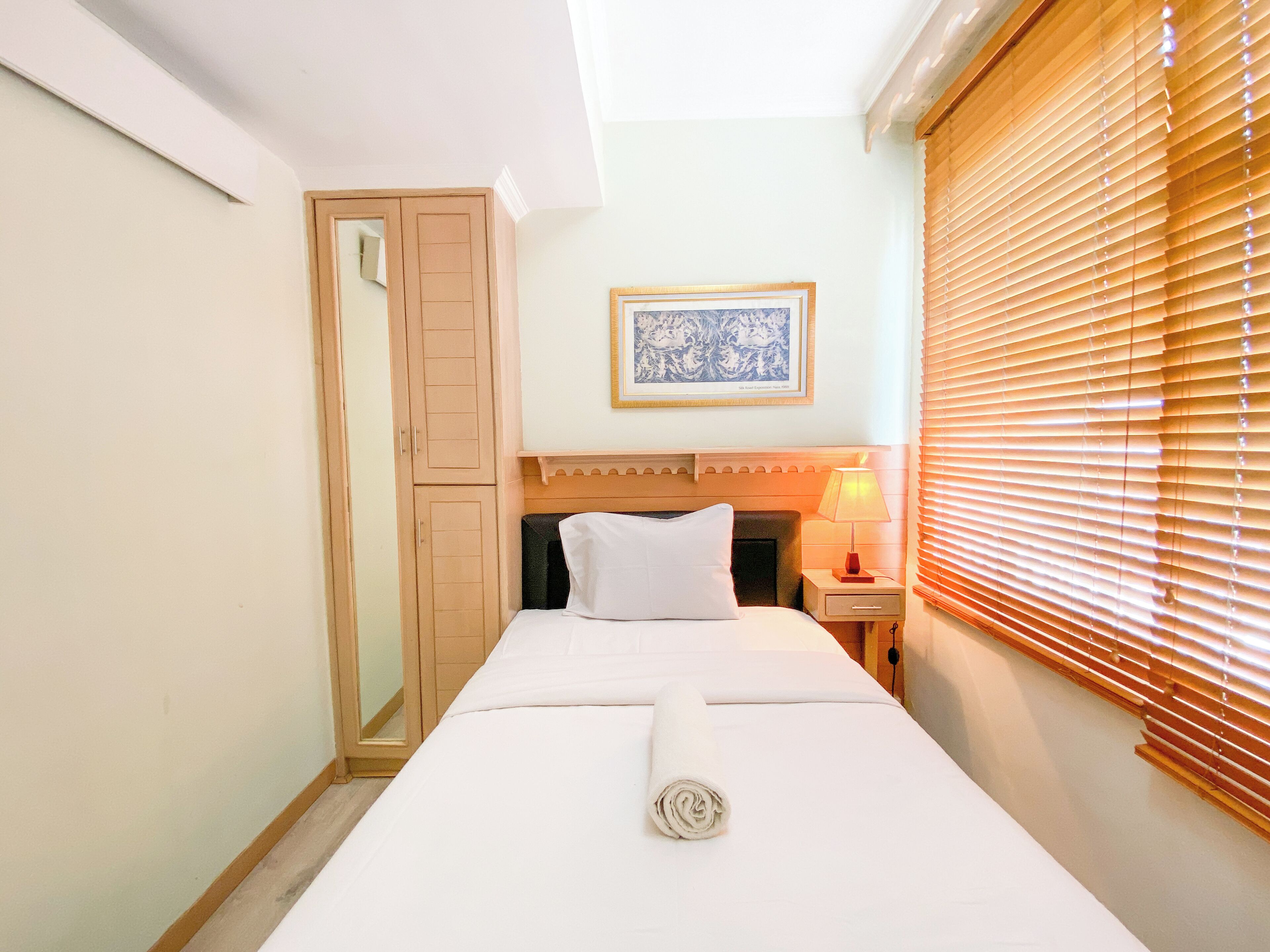 A hotel room with a bed, a nightstand, a lamp, a window with blinds, a door, and a framed picture on the wall.