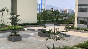 A courtyard with potted trees, a paved walkway, and modern buildings in the background. - Good Deal and Cozy Studio Daan Mogot City Apartment (Jakarta)