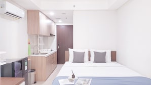 A modern hotel room with a kitchenette, a bed with two pillows, and a bedside table with a magazine and a bottle. - Good Deal and Cozy Studio Daan Mogot City Apartment (Jakarta)