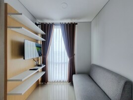 Una sala de estar moderna con un televisor de pantalla plana montado en un estante de madera, un sofá gris y un ventanal con cortinas.