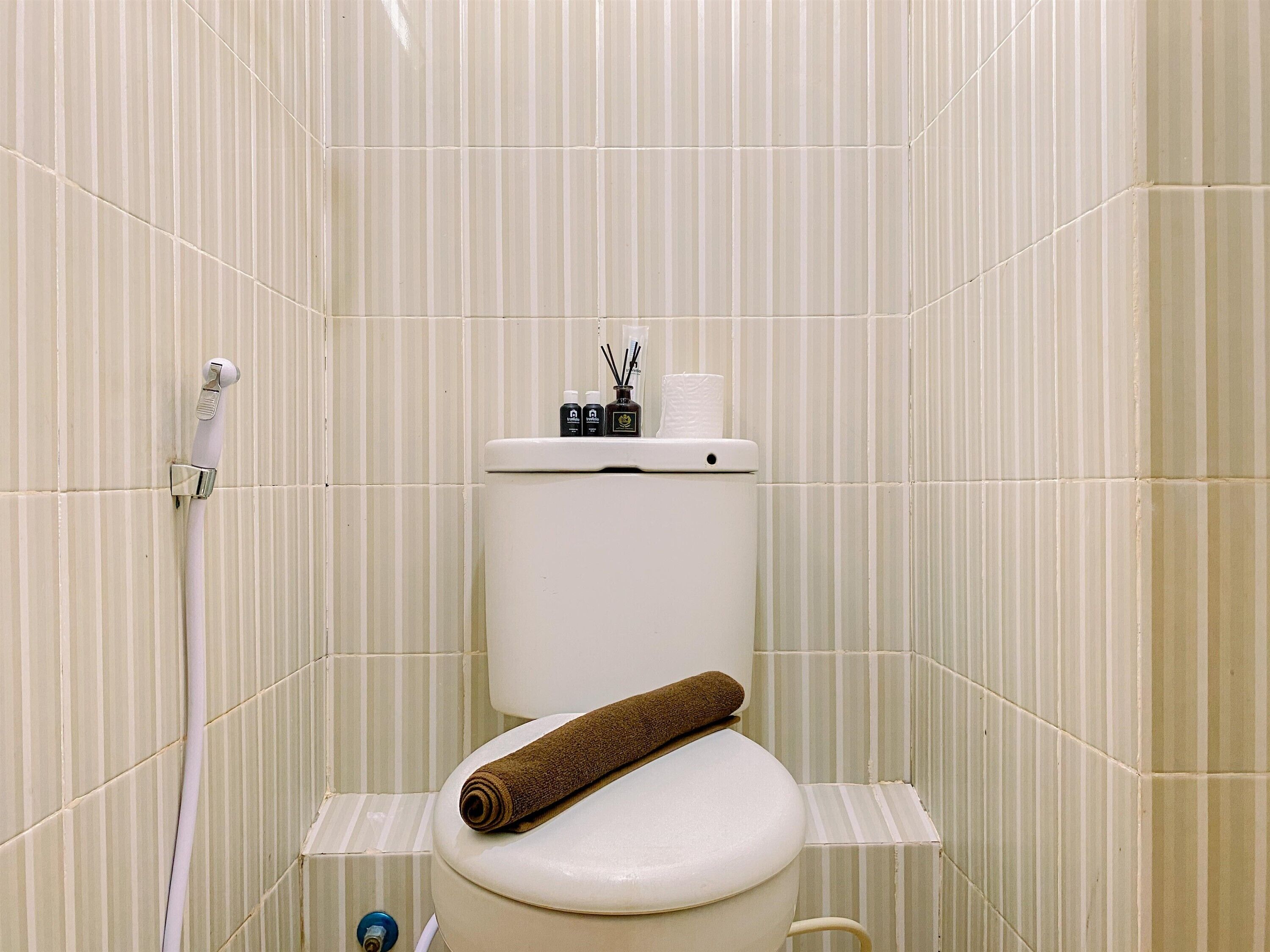 A bathroom with a toilet, a shower hose, and toiletries on the tank.