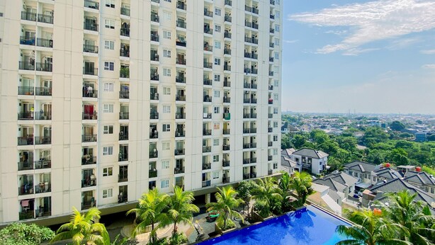 A high-rise residential building with multiple balconies, a swimming pool, and lush greenery. - Homey and Comfort Stay 2BR Cinere Resort Apartment (Depok)