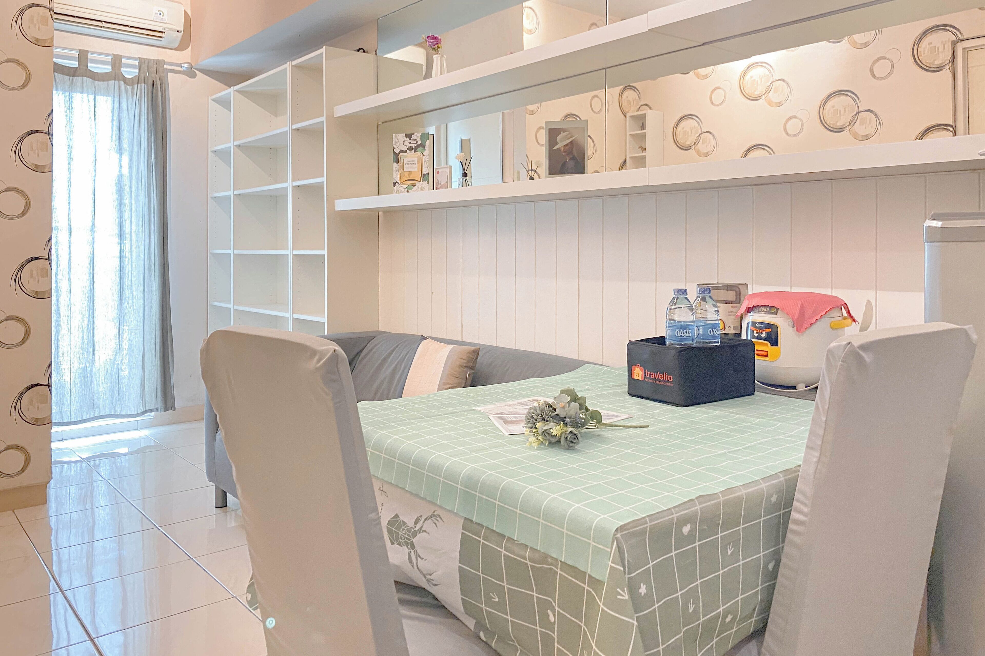 A hotel room with a bed, a table with a green checkered tablecloth, a Vello refrigerator, and a window with a curtain.