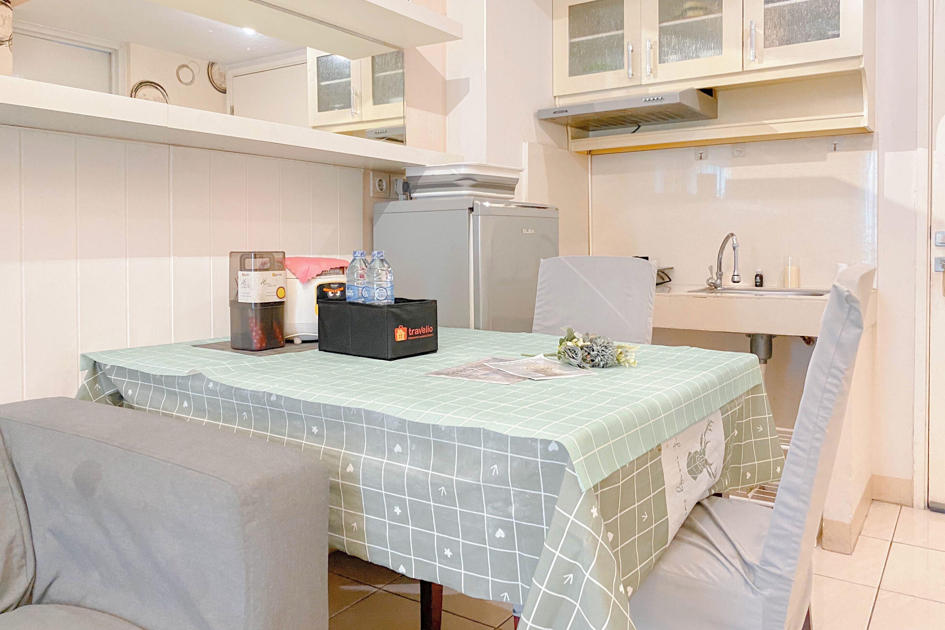 A compact kitchenette with a refrigerator, a sink, and a table with a tablecloth.
