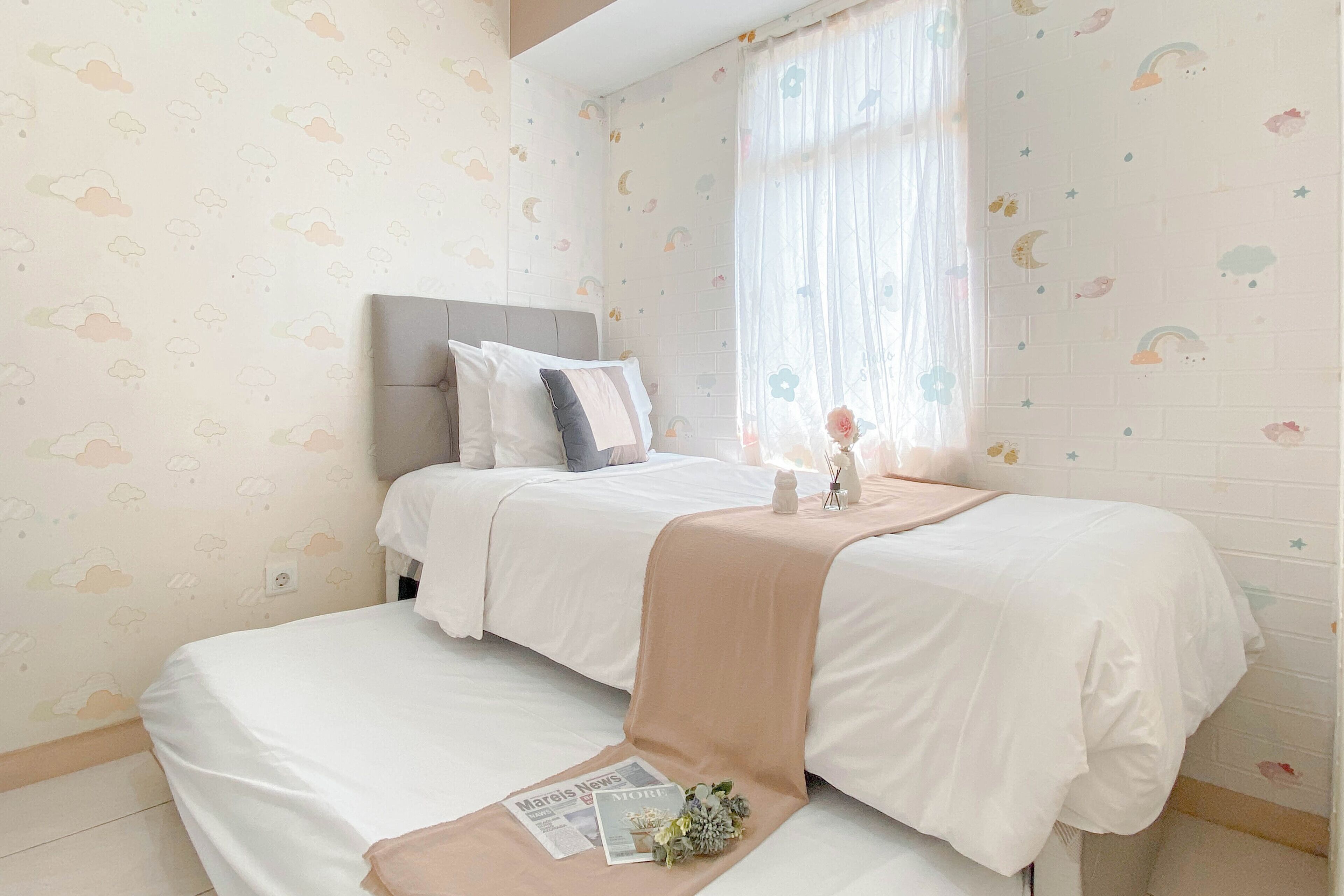 A bedroom with two beds, a window with sheer curtains, and a wall with a cloud and moon pattern.