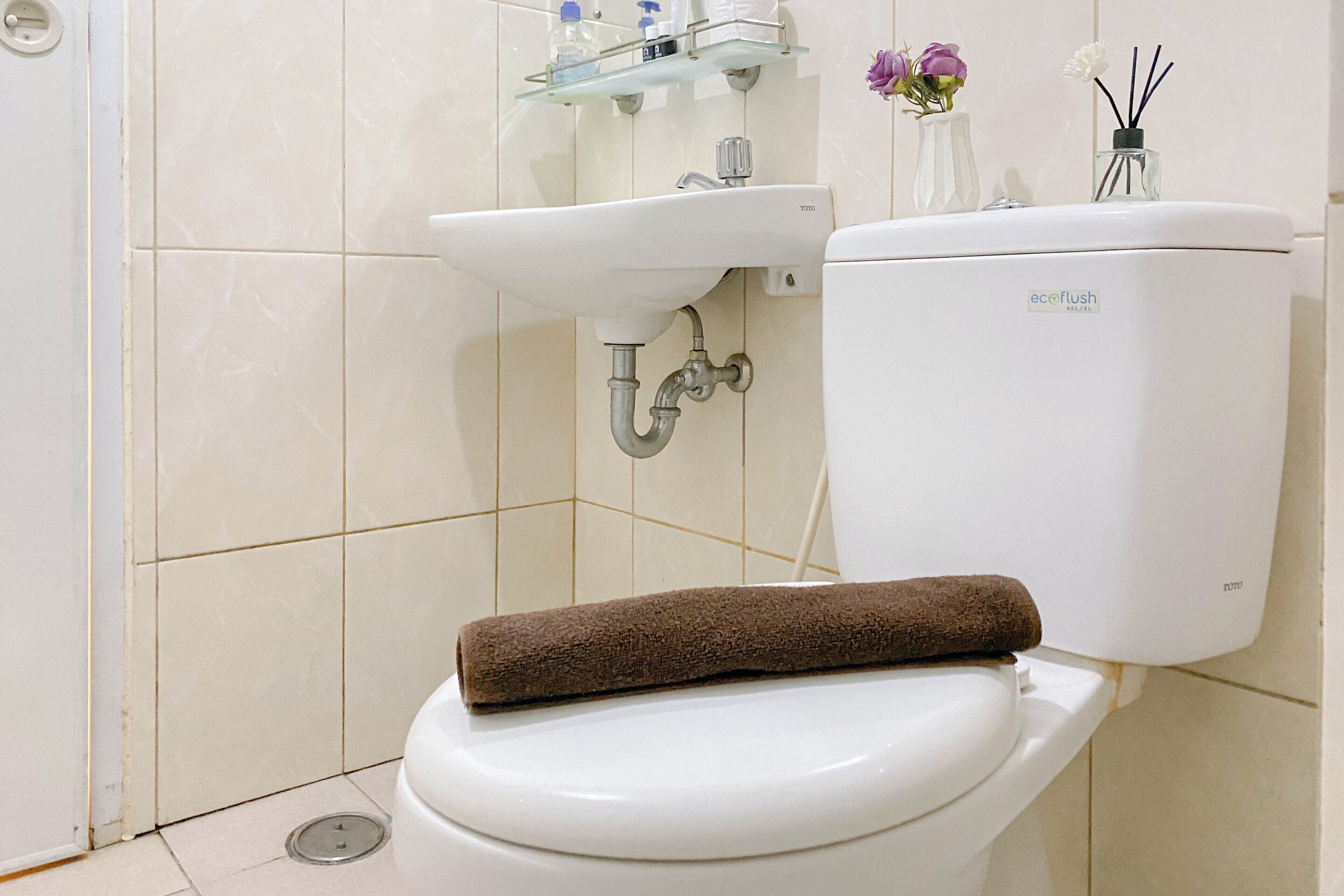 A bathroom with a toilet, a sink, and a glass shelf above the sink.