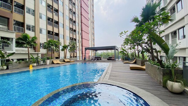 A swimming pool with a mosaic design, surrounded by lounge chairs and potted plants, with a multi-story building in the background. - Cozy and Warm Studio at LRT City Jatibening Apartment (Bekasi)