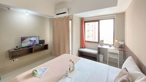 A hotel room with a bed, a desk, a television, and a window with curtains. - Cozy and Warm Studio at LRT City Jatibening Apartment (Bekasi)