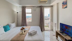 A hotel room with a bed, a TV, a window with curtains, and a view of the city. - Cozy and Simply Studio Apartment Margonda Residence 2 (Depok)