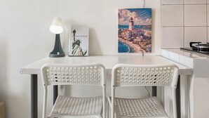 A kitchenette with a gas stove, a white table with two white chairs, a lamp, and a painting of the Statue of Liberty. - Cozy and Simply Studio Apartment Margonda Residence 2 (Depok)