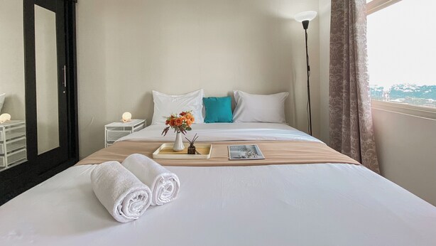 A neatly made bed with white linens, a teal pillow, and a small vase with flowers. - Cozy and Simply Studio Apartment Margonda Residence 2 (Depok)