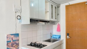 A modern kitchen with white cabinets, a gas stove, a sink, and a wooden door. - Cozy and Simply Studio Apartment Margonda Residence 2 (Depok)