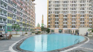 A swimming pool surrounded by residential buildings with balconies, a mosque with a minaret in the background, and a few people around the pool area. - Cozy and Simply Studio Apartment Margonda Residence 2 (Depok)