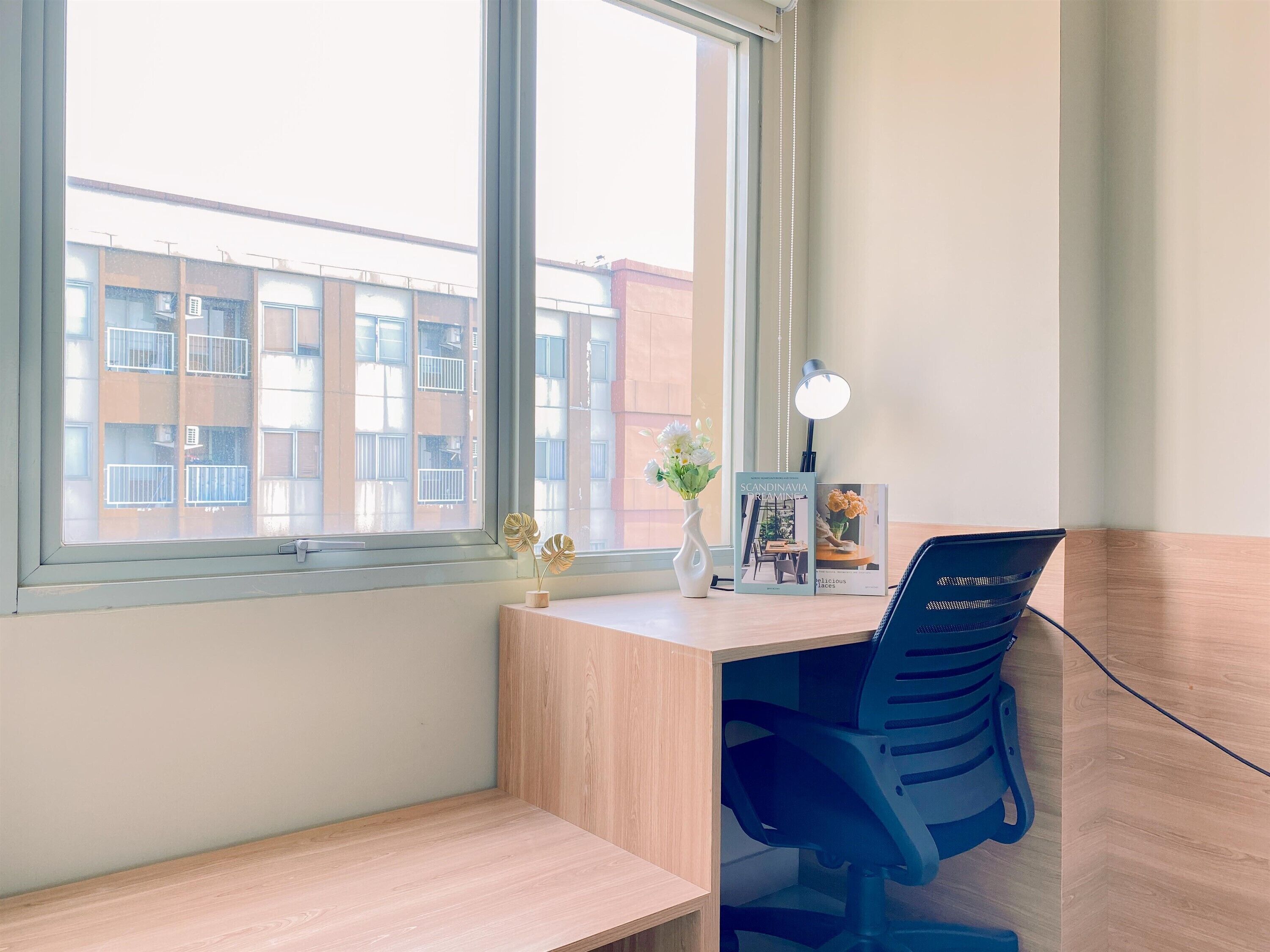Een compact, overzichtelijk werkplekje met een bureau, stoel en een raam met uitzicht op een gebouw.