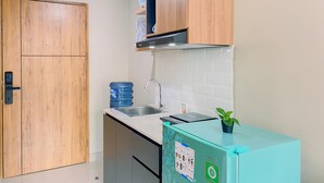 A compact kitchen with wooden cabinets, a stainless steel sink, a blue water dispenser, and a small refrigerator. - Cozy Living Studio at LRT City Jatibening Apartment (Bekasi)