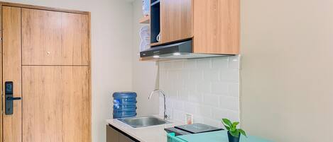A compact kitchen with wooden cabinets, a stainless steel sink, a blue water dispenser, and a small refrigerator.