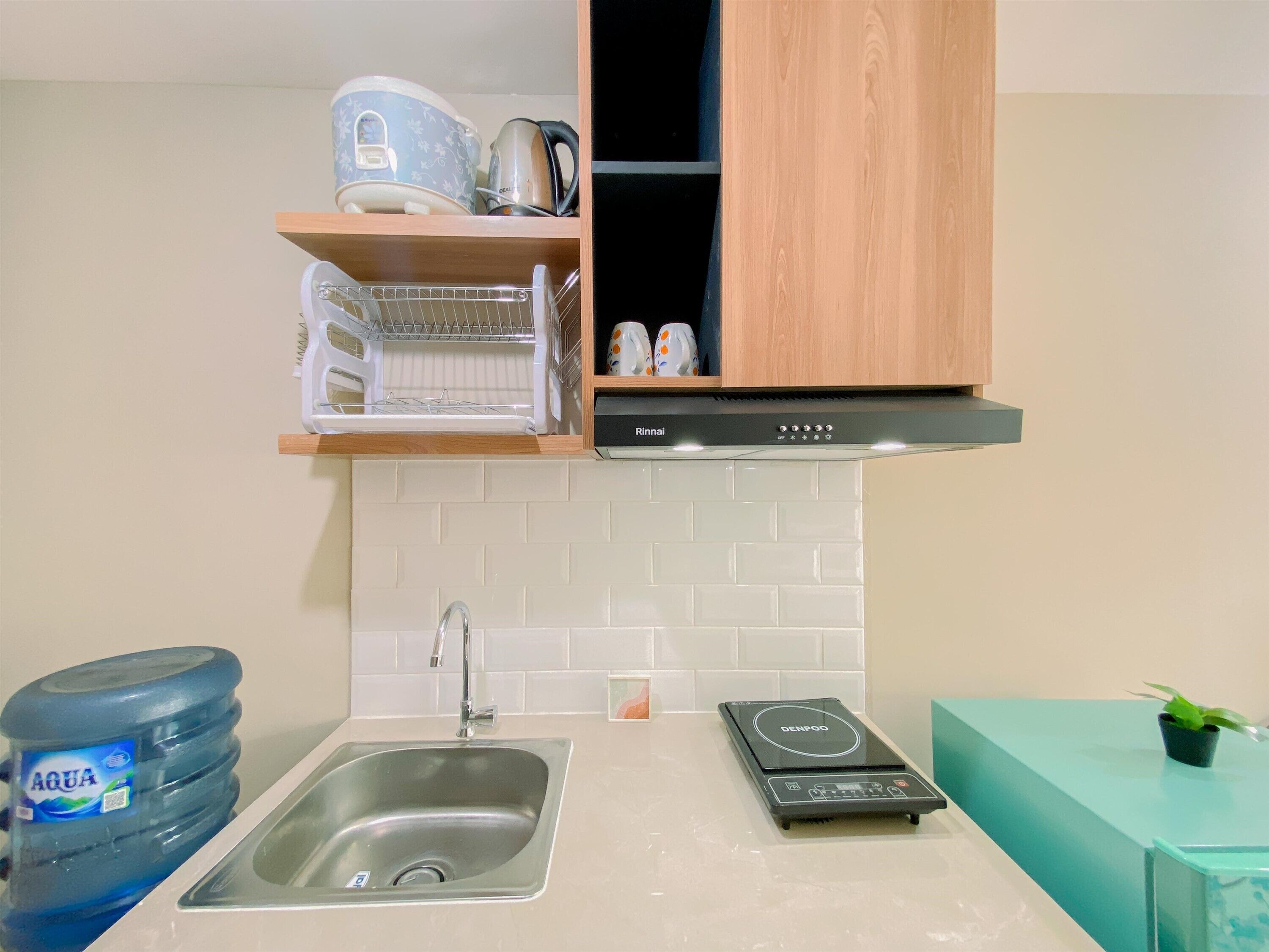 Une cuisine équipée d’un évier, d’un distributeur d’eau, d’un cuiseur à riz et d’un petit plan de travail agrémenté d’une plante.