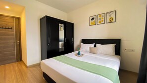 A hotel room with a bed, a wardrobe, and three framed artworks on the wall.
