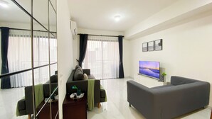 A modern living room with a grey sofa, a flat-screen TV, and a large window with sheer curtains.