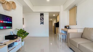 Uma sala de estar moderna com uma televisão de tela plana, um sofá, uma mesa de centro e uma área de cozinha ao fundo.