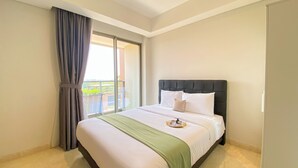 A hotel room with a bed, a green throw blanket, and a view of a balcony. - Great Location and Homey Studio Gold Coast Apartment near PIK (Jakarta)