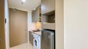 A compact kitchen with a washing machine, a refrigerator, and a small countertop. - Great Location and Homey Studio Gold Coast Apartment near PIK (Jakarta)