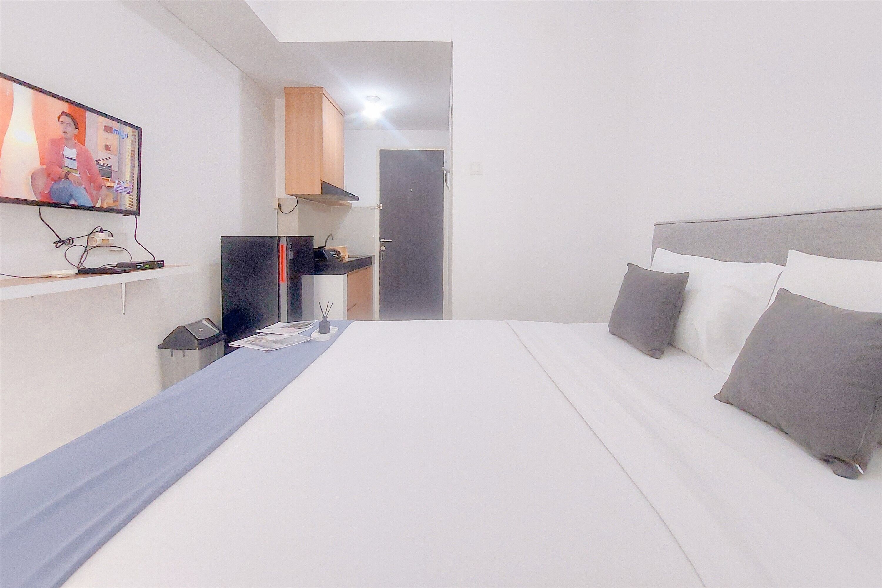 A hotel room with a bed, a television, a desk with a computer, and a door.