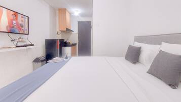A hotel room with a bed, a television, a desk with a computer, and a door.