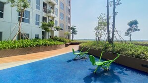 Un espace piscine sur le toit, doté d’un sol bleu, de chaises d’exercice vertes et offrant une vue sur un immeuble avec des balcons et de la verdure.