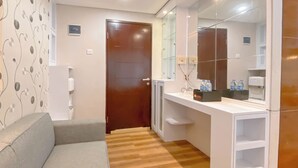 Ein Hotelzimmer mit Holzboden, einem grauen Sofa, einem weißen Konsolentisch mit Spiegel und einer Tür.