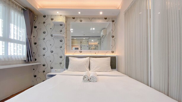 A modern hotel room with a neatly made bed, a large mirror, and a window with curtains.