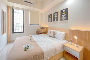 A hotel room with a bed, bedside table, lamp, artwork, and a window with a view of buildings. - Cozy Living Studio at Evenciio Margonda Apartment (Depok)