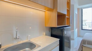 A modern kitchen with a stainless steel sink, a black refrigerator, and wooden cabinets. - Cozy Living Studio at Evenciio Margonda Apartment (Depok)