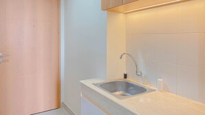 A modern kitchen with a stainless steel sink, wooden cabinets, and a light-colored countertop. - Cozy Living Studio at Evenciio Margonda Apartment (Depok)