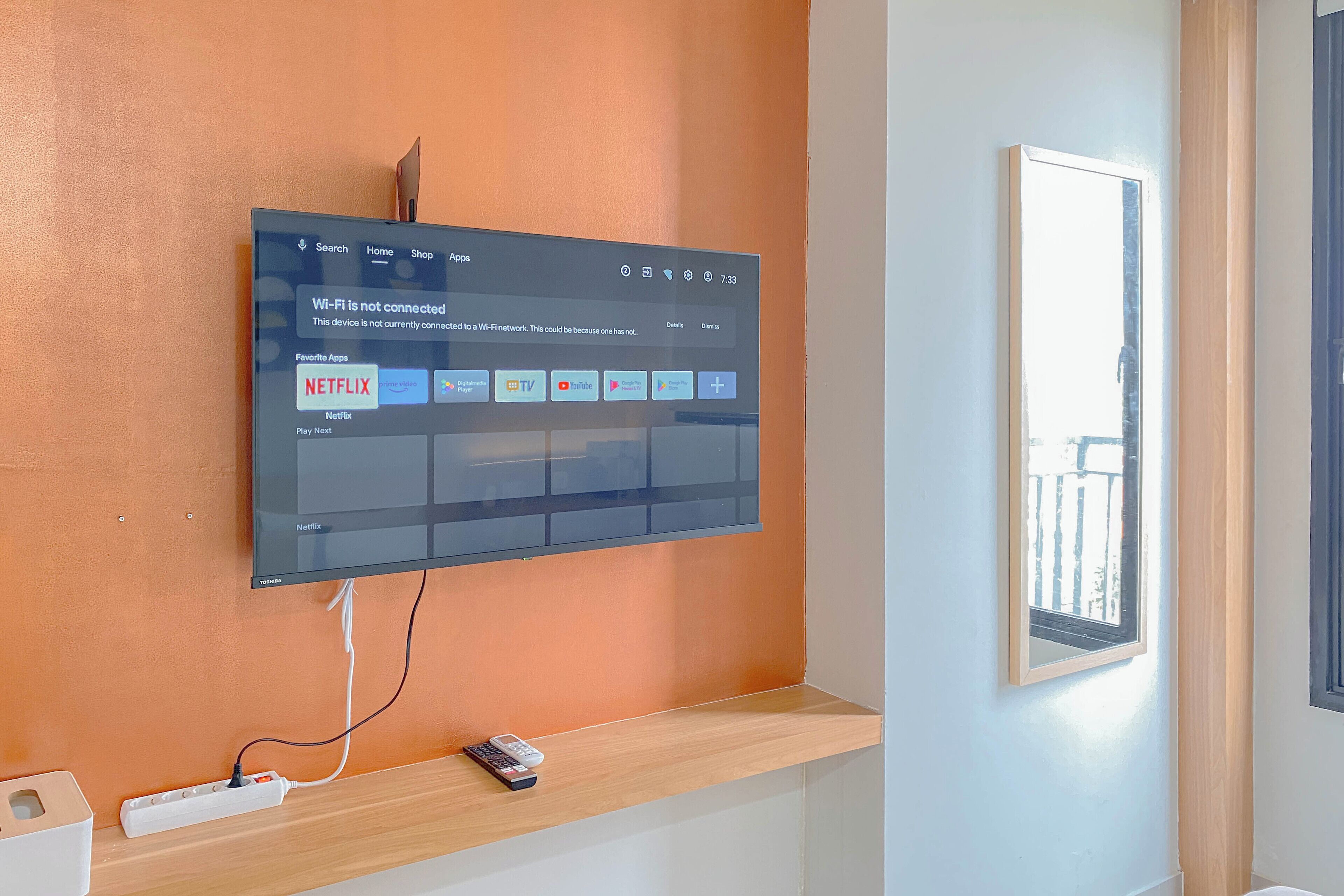 A flat-screen TV mounted on an orange wall displaying a Wi-Fi connectivity issue and a Netflix app.