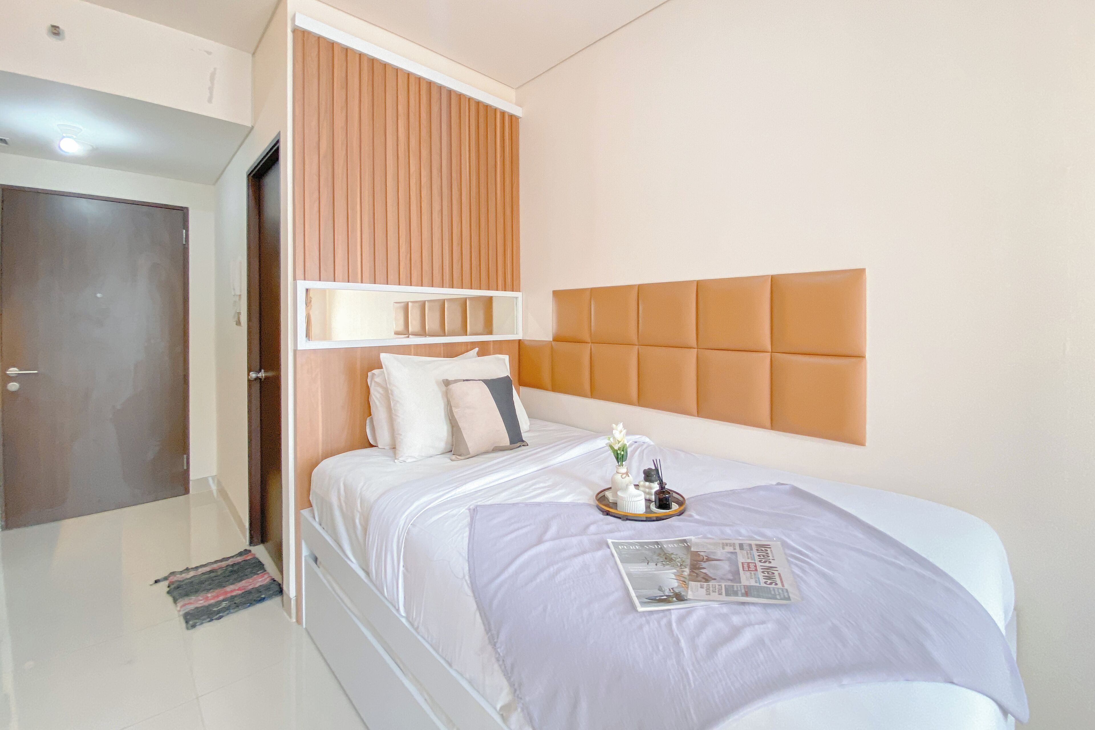 Un dormitorio ordenado con cama, almohadas, una bandeja con artículos de aseo y una revista sobre la cama.