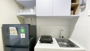 A compact kitchen with a black refrigerator, a built-in induction cooktop, a sink, and white cabinetry. - Minimalistic and Cozy Studio Amartha View Apartment (Semarang)