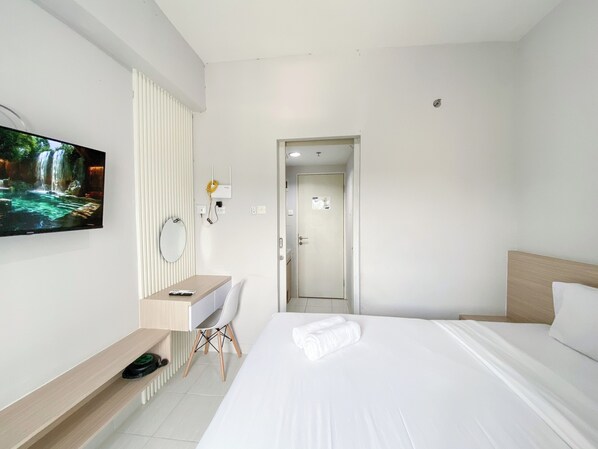 Ein modernes Hotelzimmer mit einem großen Bett, einem Schreibtisch mit Stuhl, einem Flachbildfernseher und einer Badezimmertür.