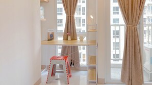 A modern room with a large window, a small red and white stool, and a shelf with a vase and a lamp. - Homey Studio Apartment at Tokyo Riverside PIK 2 (Teluknaga)