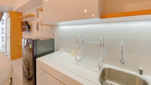 A modern kitchen with white tiles, stainless steel appliances, and a built-in sink. - Homey Studio Apartment at Tokyo Riverside PIK 2 (Teluknaga)