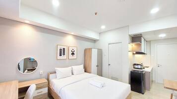 A modern hotel room with a bed, bedside table, chair, and a kitchenette area.